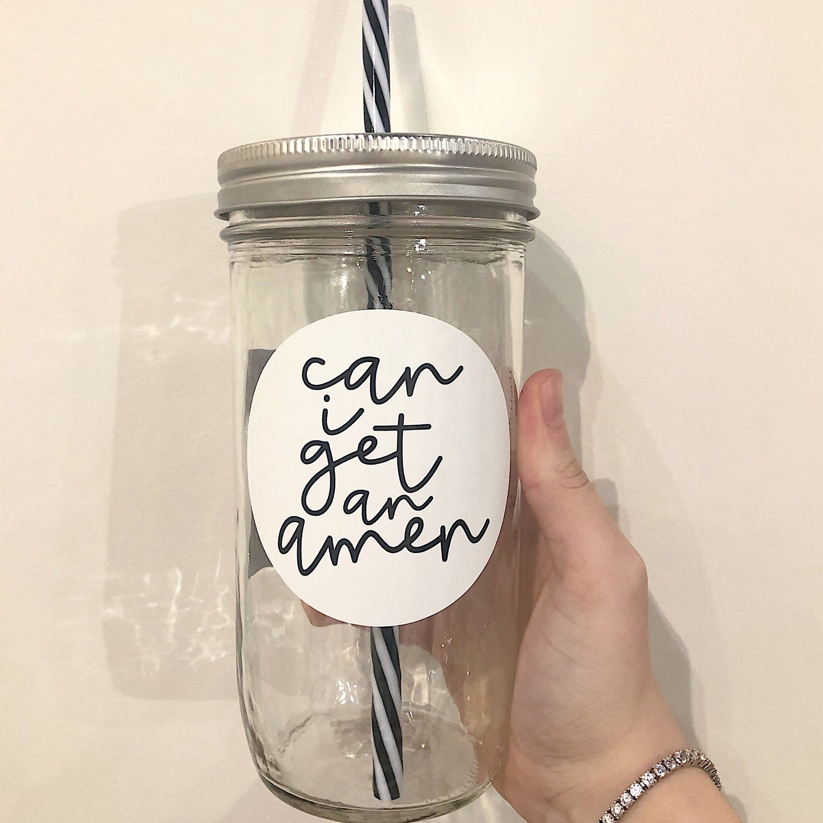 Hand holding a mason jar tumbler that has a white circular decal that has “can I get an amen” written in black on it.
