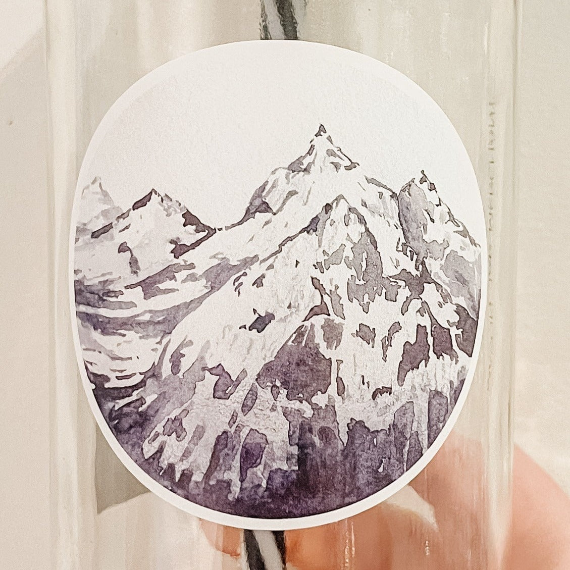 Close up of a hand holding a mason jar tumbler that has a circle decal of a snowy mountain peak.