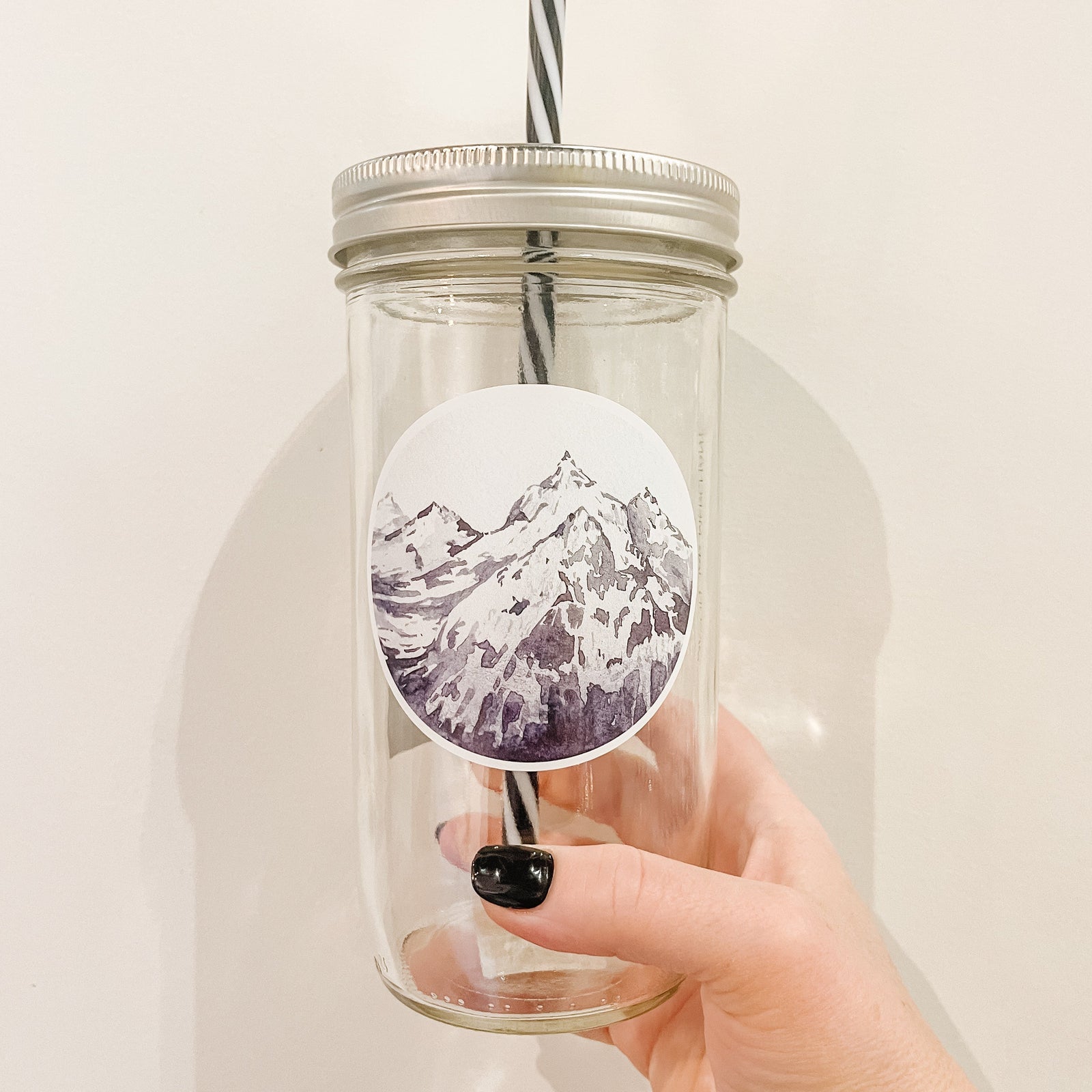 Hand holding a mason jar tumbler that has a circle decal of a snowy mountain peak.