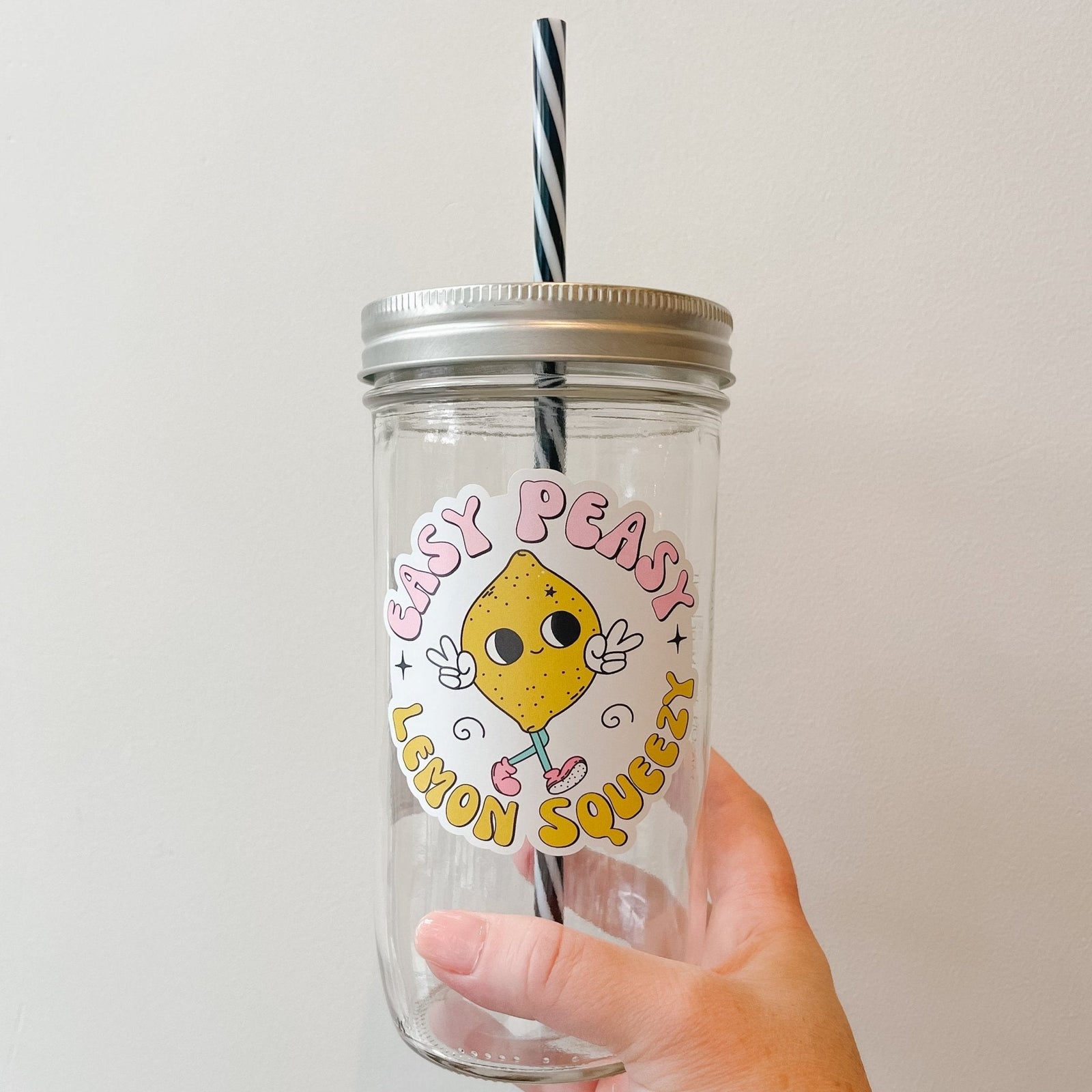 Hand holding a mason jar tumbler that says “Easy peasy lemon squeezy” with a lemon character giving 2 peace signs.
