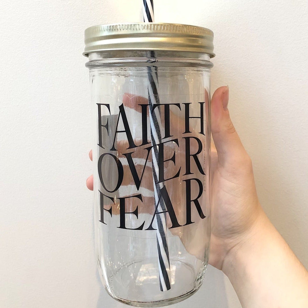 Hand holding a mason jar tumbler that says “faith over fear”