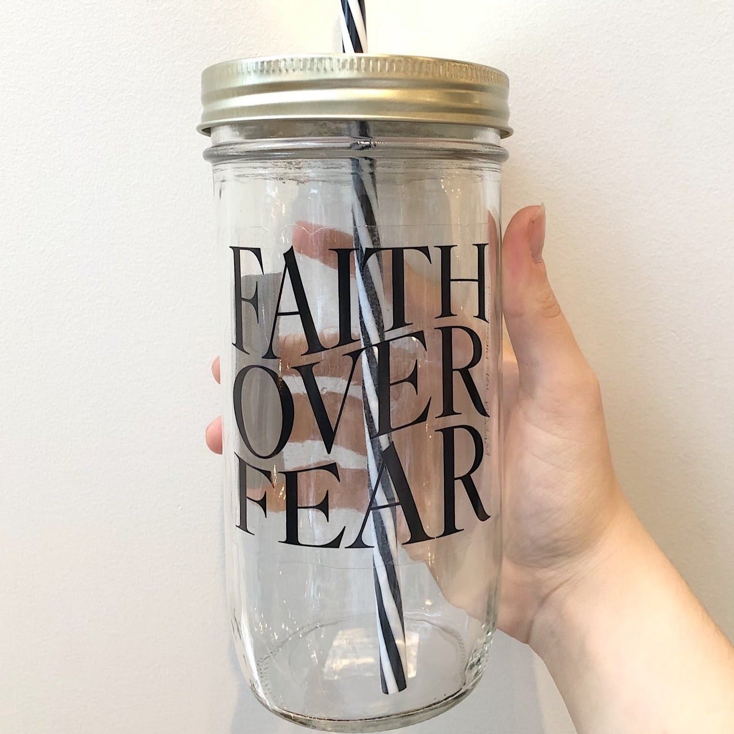 Hand holding a mason jar tumbler that says “faith over fear”