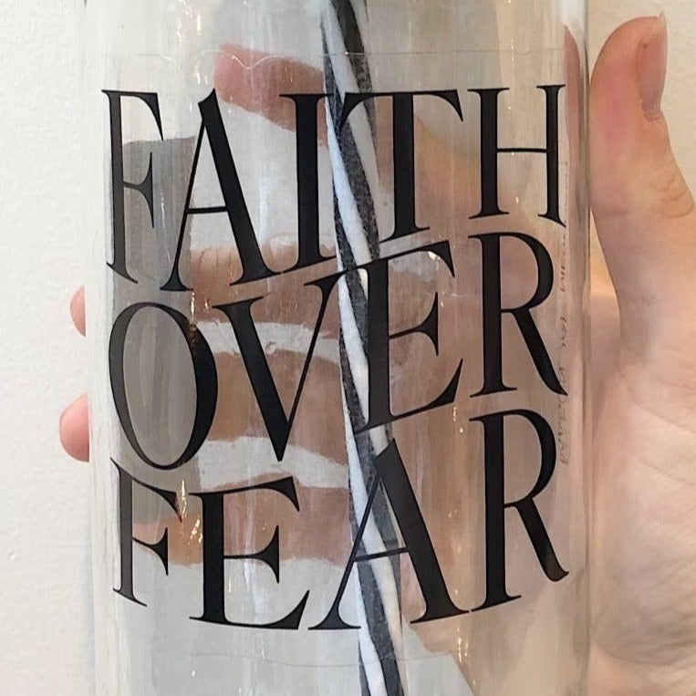 Close up of a hand holding a mason jar tumbler that says “faith over fear”