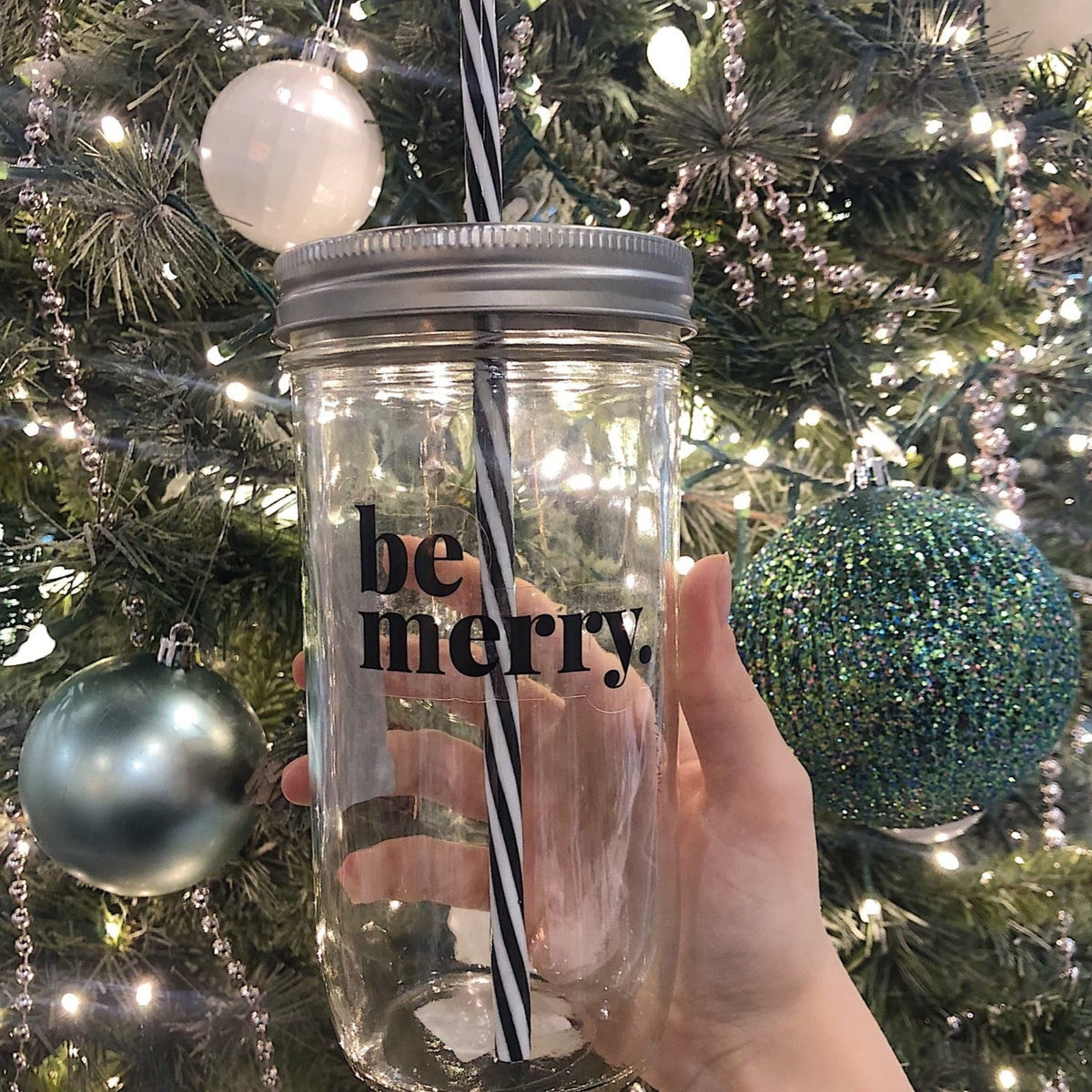 Hand holding a mason jar tumbler that says "be merry.”