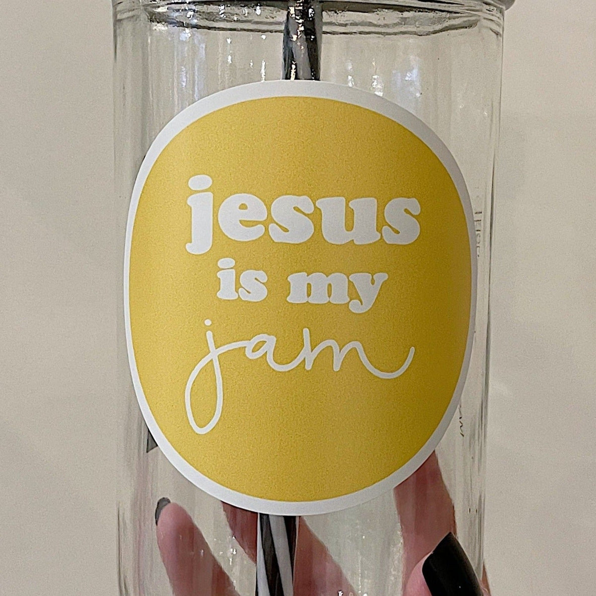 Close up of a mason jar tumbler that has a yellow circular decal with the words “Jesus is my jam” written in the circle in white.