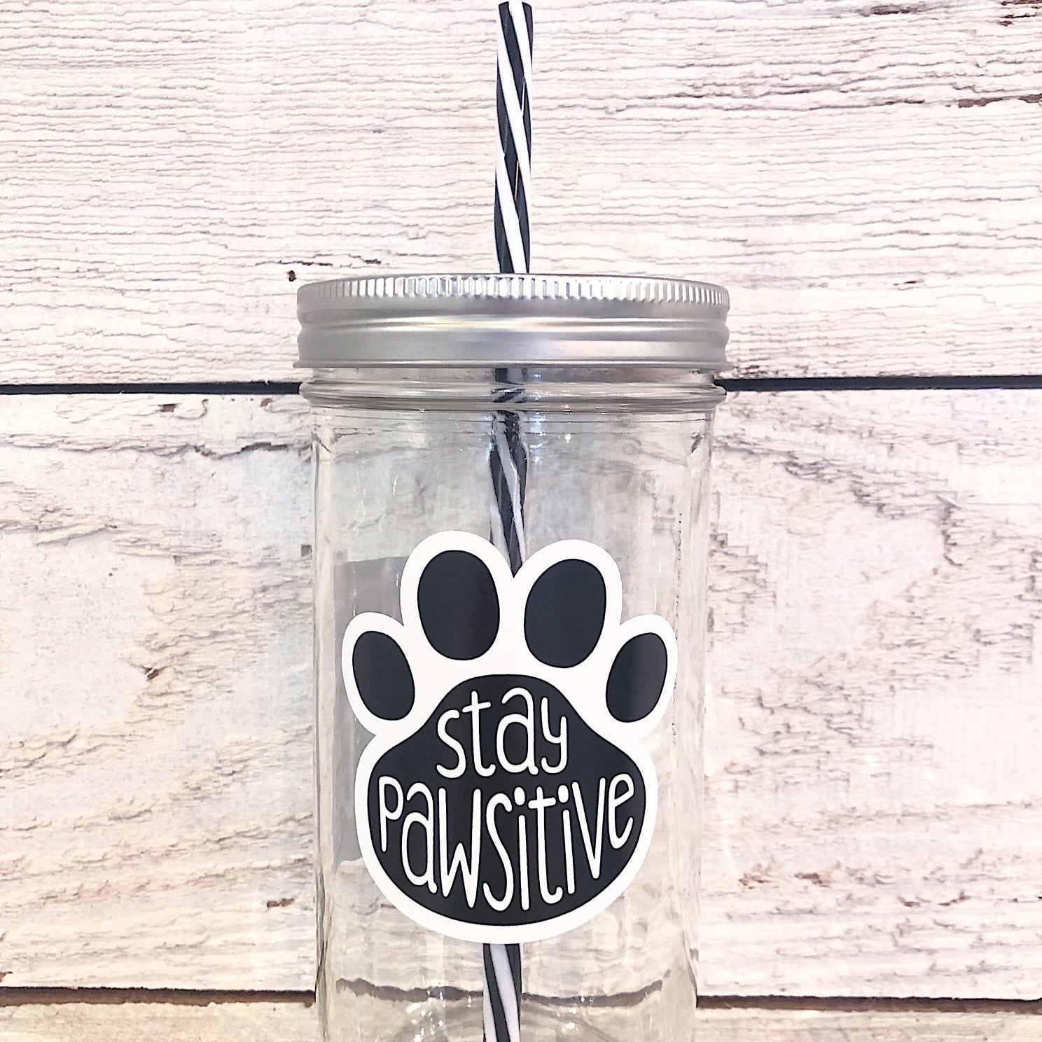 Mason jar tumbler that has a black paw print and in the paw print says “stay pawsitive”
