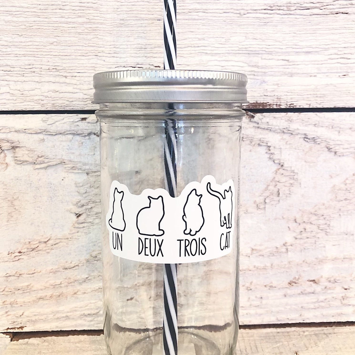 A mason jar tumbler that says “un deux trois cat” with a different outline of a cat over each word