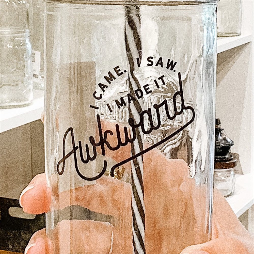 Photo of Mason Jar Tumbler with a gold lid and black and white spiral pattern straw. Mason Jar has a vinyl decal. Photographed against shelves with different mason jars.