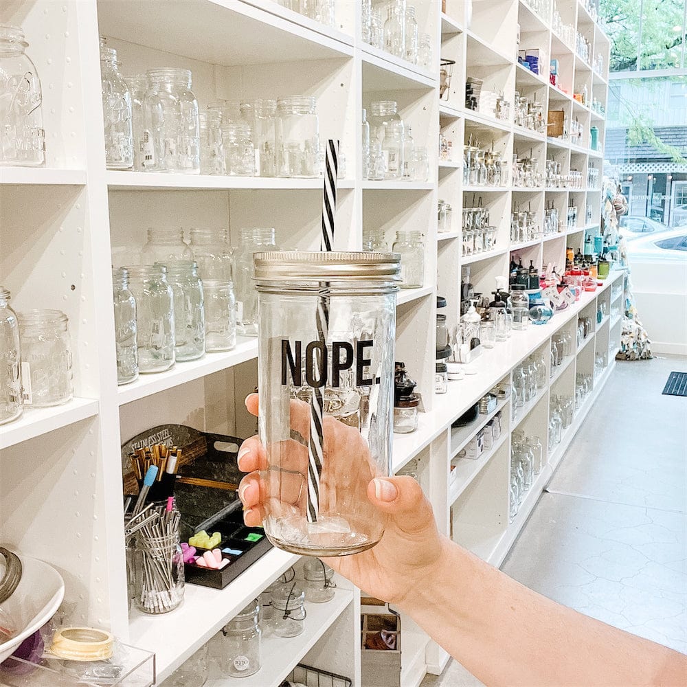 Wide angle of a hand holding a mason jar tumbler that says “NOPE.” In a mason jar store
