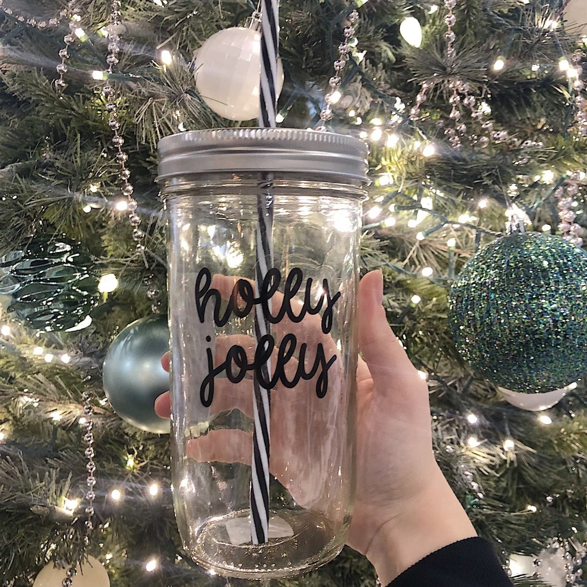 A hand holding a mason jar tumbler that says “holly jolly”
