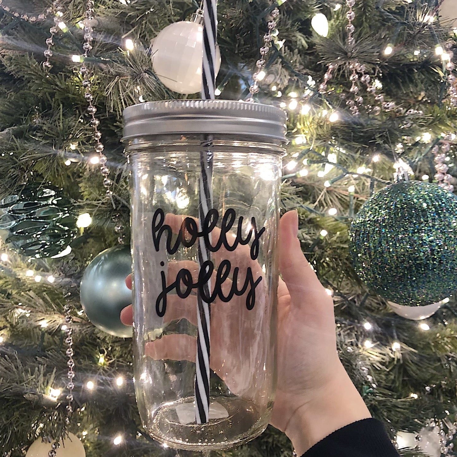 A hand holding a mason jar tumbler that says “holly jolly”