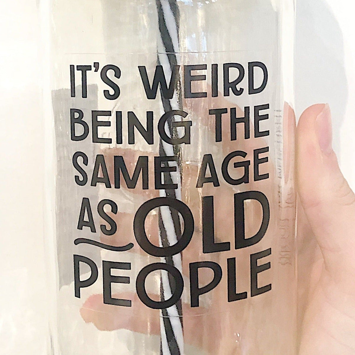 Close up of a hand holding a mason jar tumbler that says “It’s weird being the same age as old people”