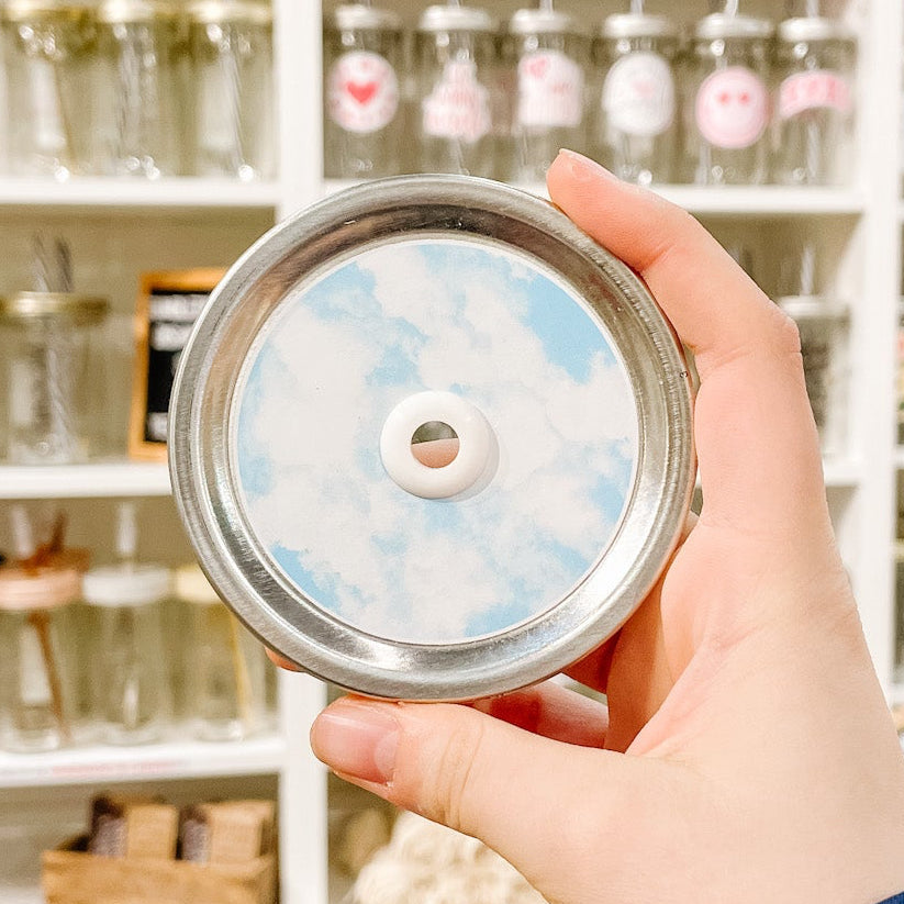 Hand holding mason jar patterned straw lid with a cloudy watercolour design on light blue background