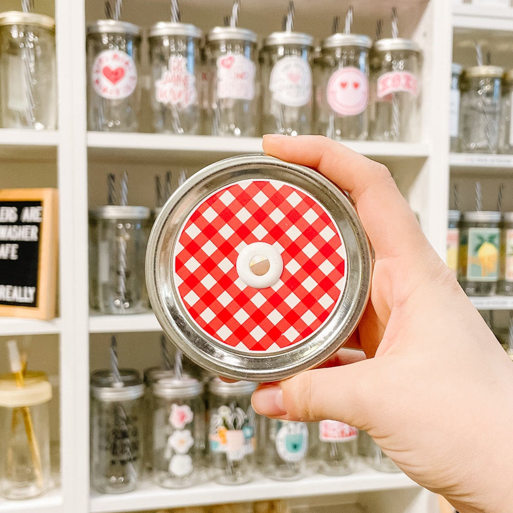 Hand holding mason jar patterned straw lid with red and white gingham design.
