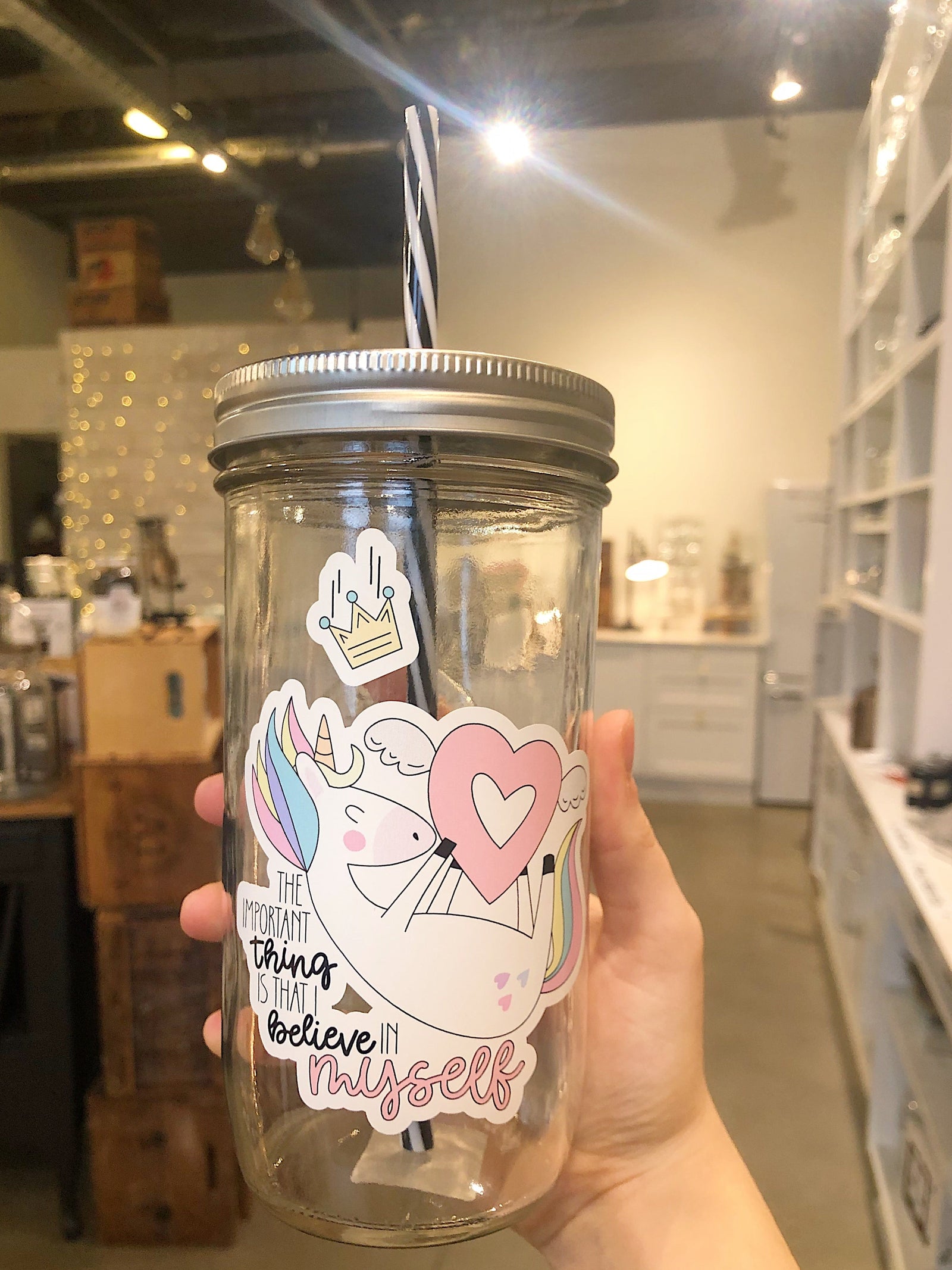 Hand holding a mason jar tumbler that says “the important thing is that I believe in myself” with a picture of a unicorn.