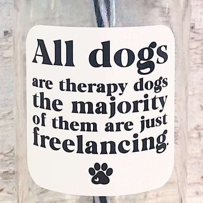 Close up of a mason jar tumbler that says “All dogs are therapy dogs the majority of them are just freelancing.” In black letters on a white background with a small black paw print at the bottom.