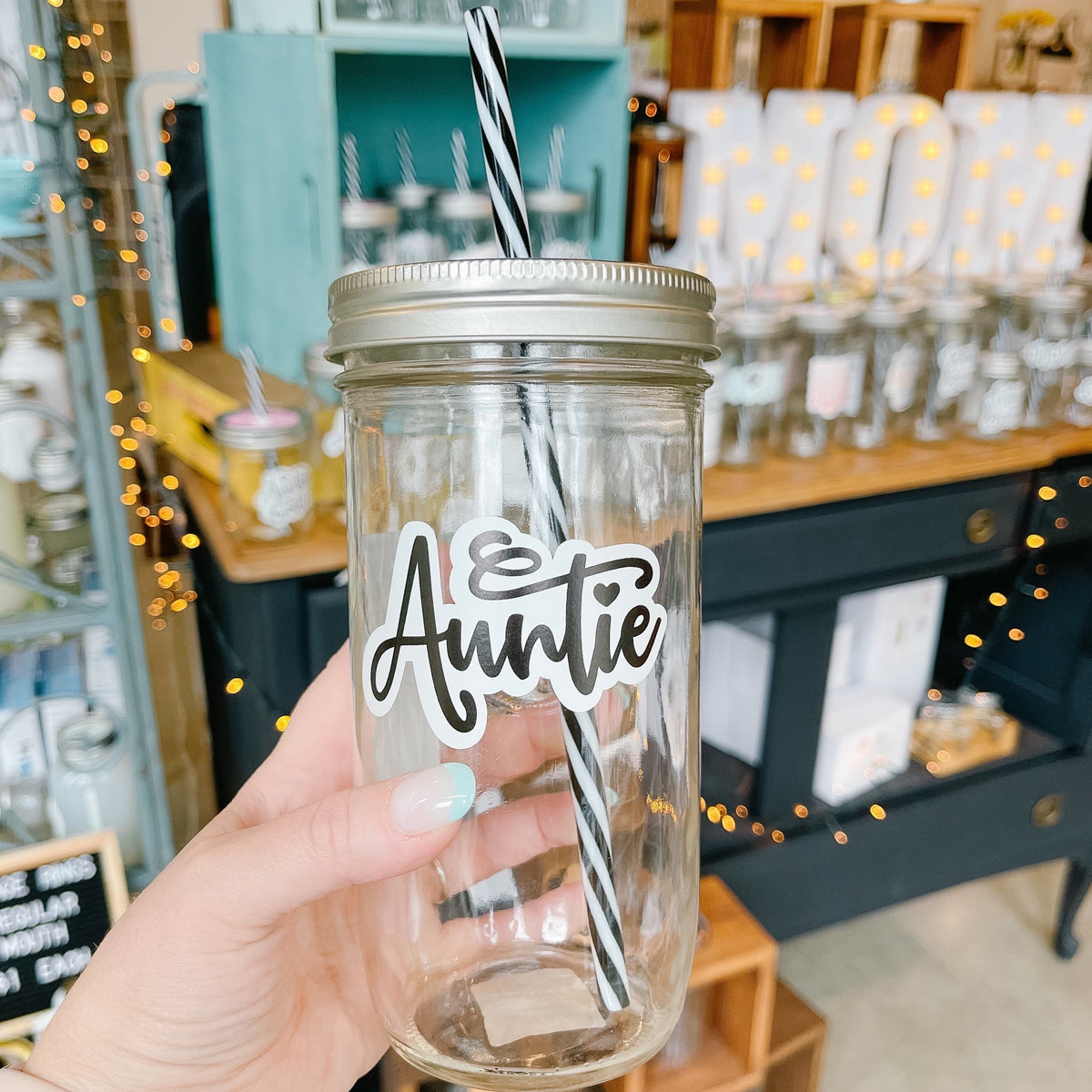 Hand holding a mason jar tumbler that says “Auntie” in script with the I dotted with a heart.