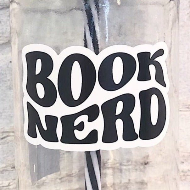 Flat lay of a mason jar tumbler that says "book nerd”, a straw lid with images of various reading glasses, and a black and white striped straw.