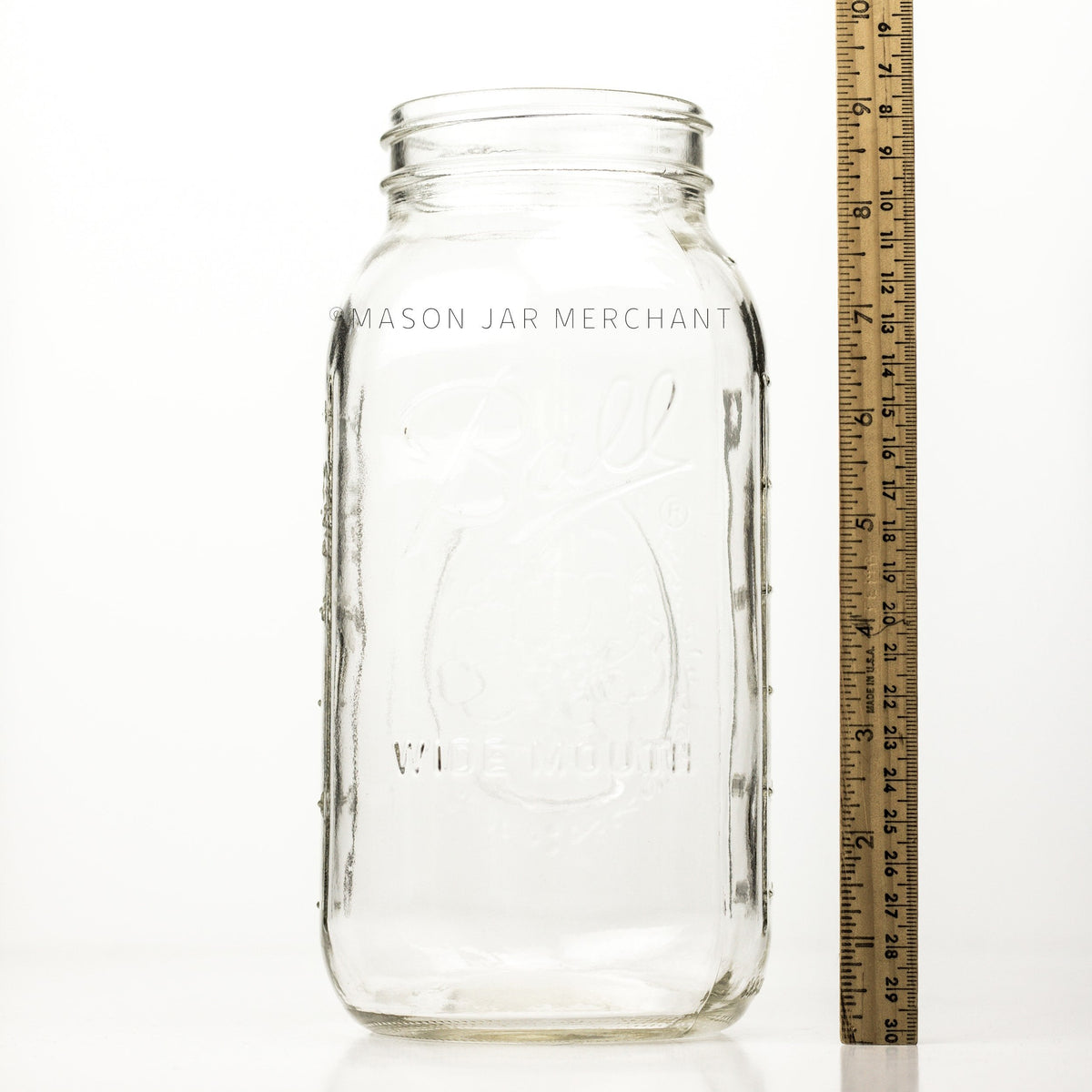 Wide mouth half-gallon mason jar with Ball Wide mouth logo, and fruity oval design visible on the back side of the jar. against a white background together with a meter stick beside it