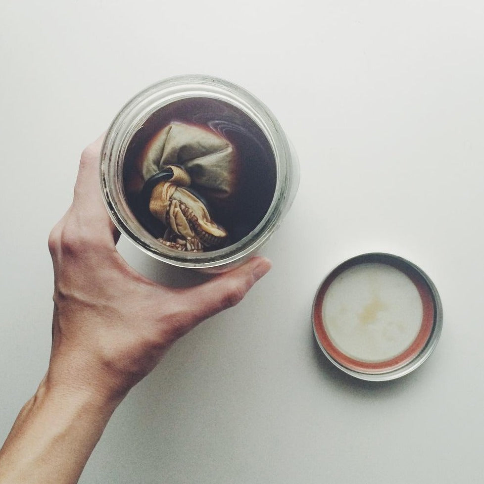Top-down photograph of a mason jar filled with coffee and a coffee filter inside with the lid against a white background.