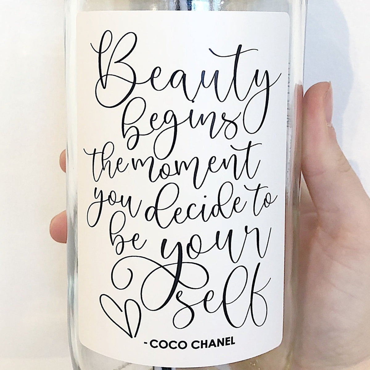 Close up of a hand holding a mason jar tumbler that says “beauty begins the moment you decide to be your self -Coco Chanel”