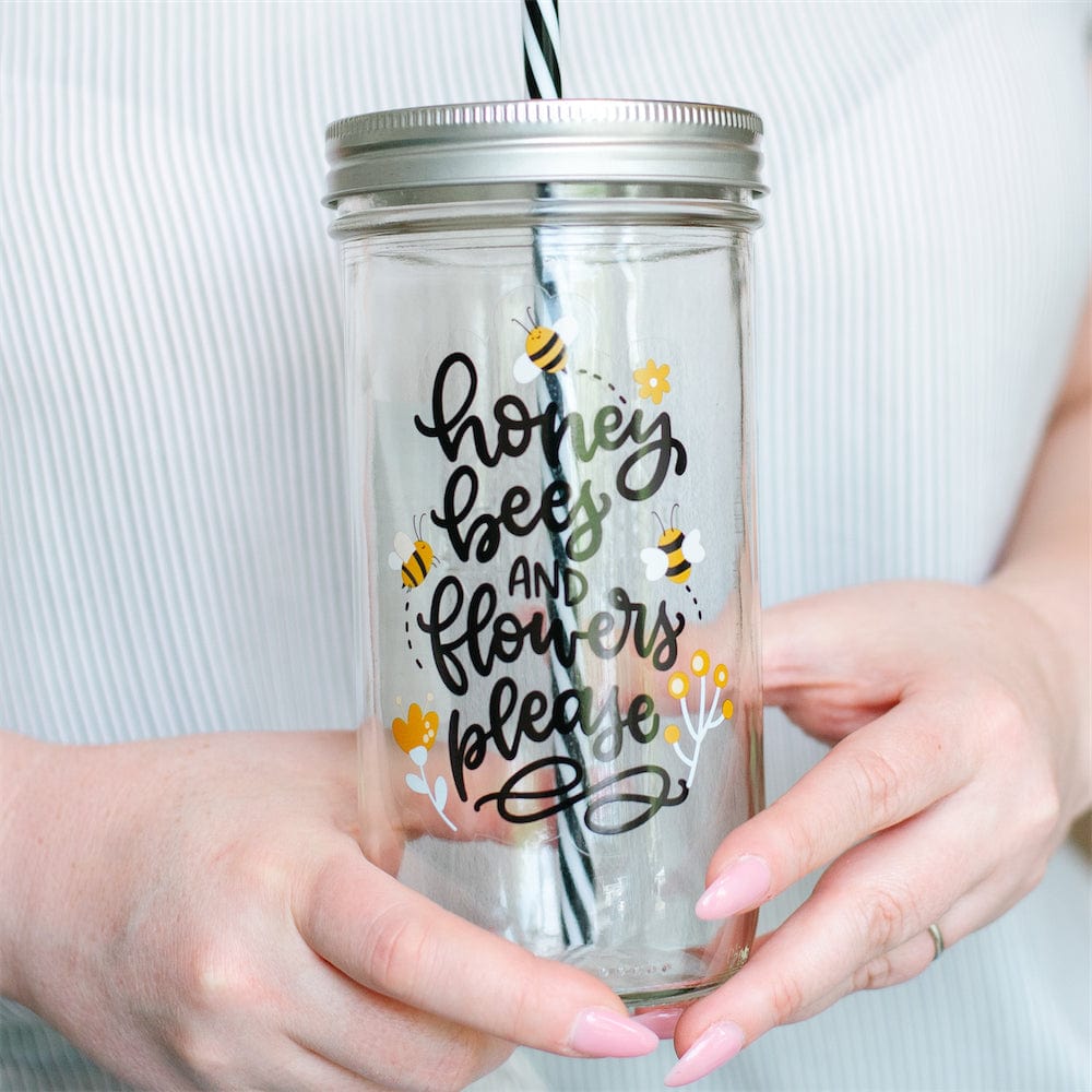 A close up of a Photo of a mason jar tumbler with a print that says "honey, bees, and flowers please".