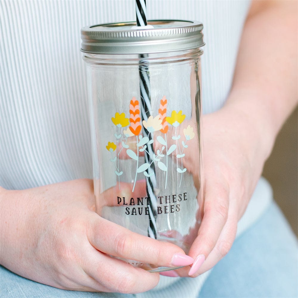 A close up of a Photo of a mason jar tumbler with a print of flowers and a text that says "plant these, save bees'.