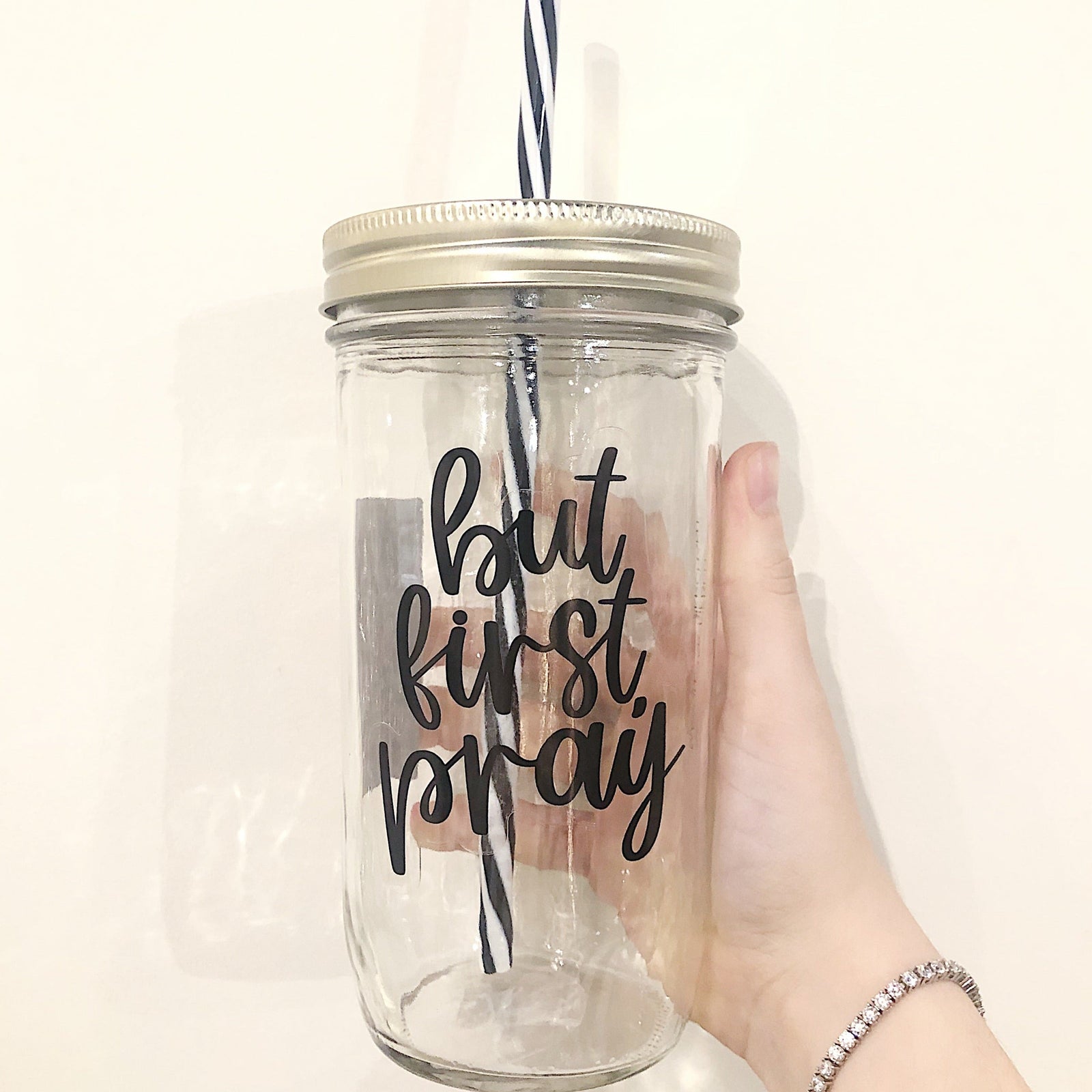 Hand holding a mason jar tumbler that says "but first, pray”