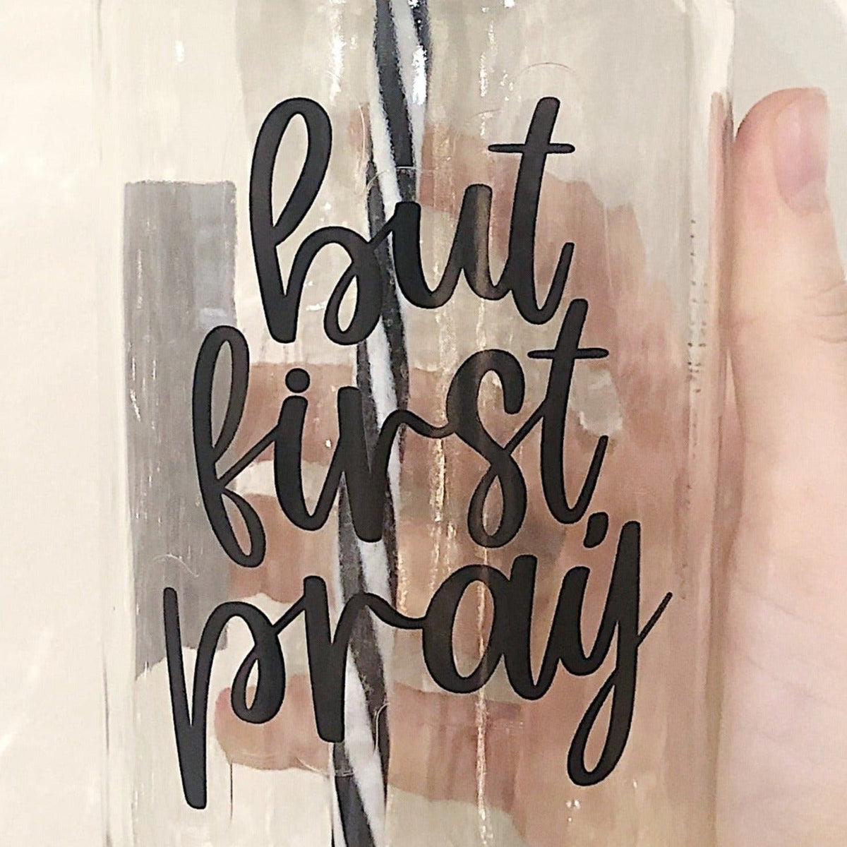 Close up of a hand holding a mason jar tumbler that says “but first, pray”