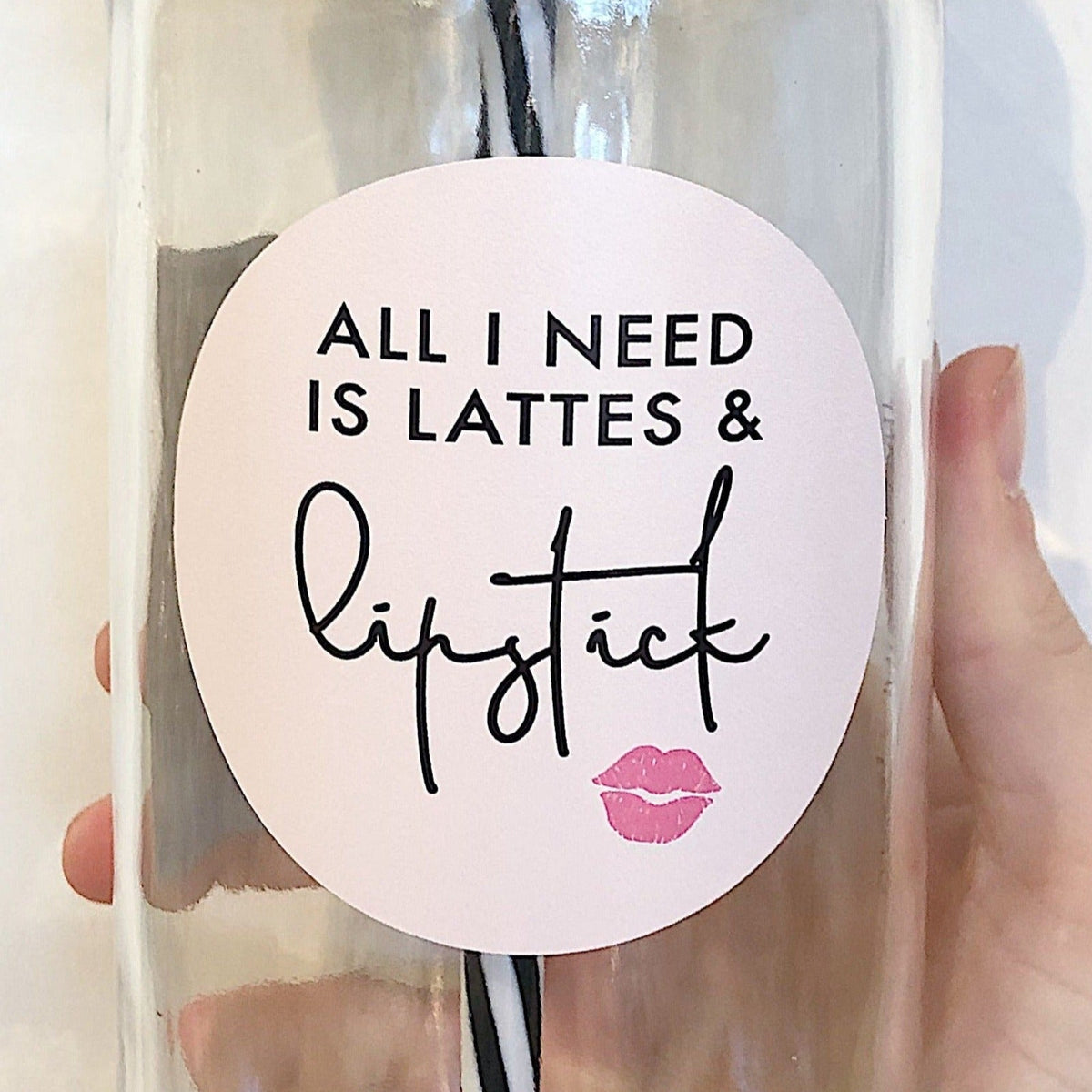 Close up of a hand holding a mason jar tumbler that says “all I need is lattes & lipstick”