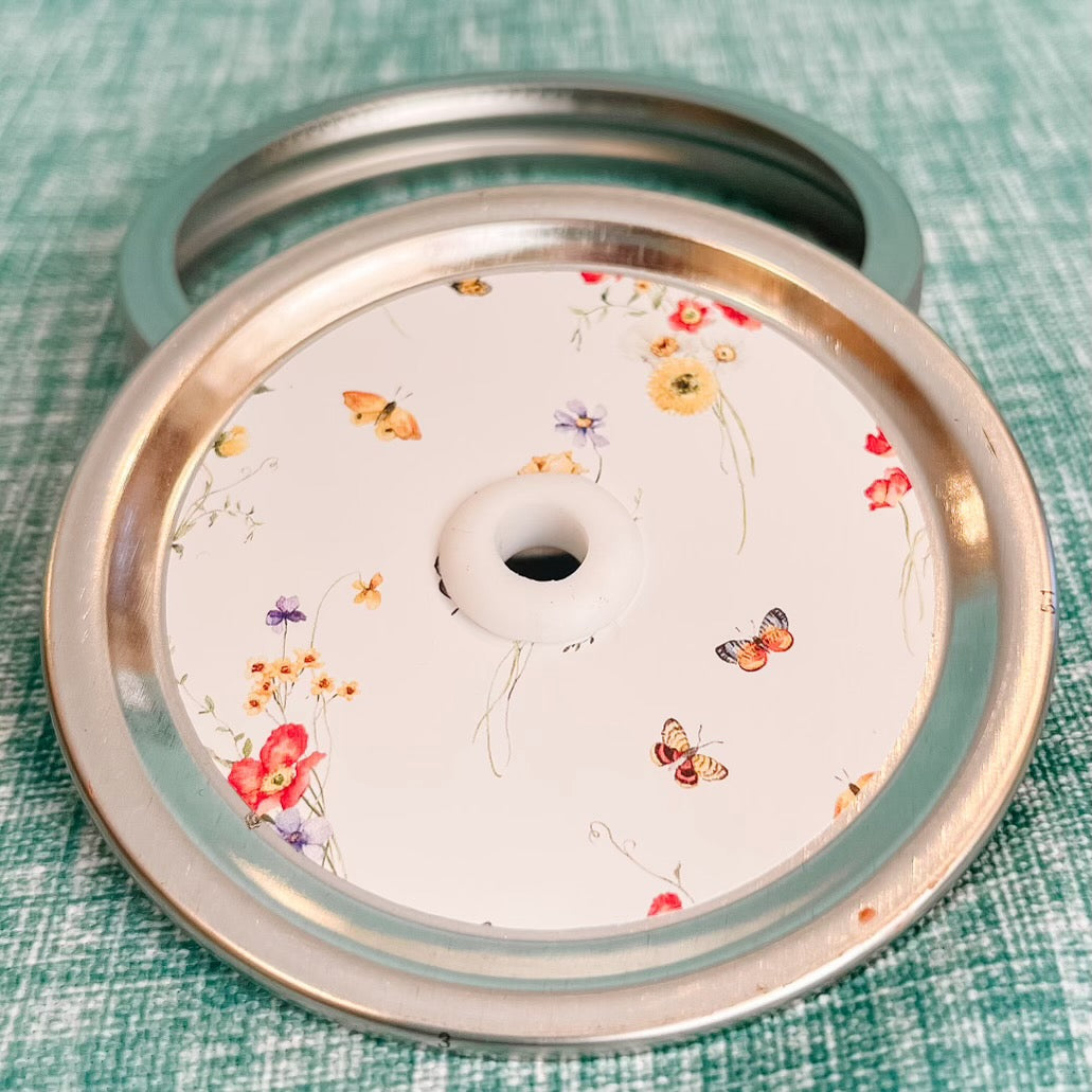 close up of a straw lid with a white background, bundles of flowers and butterflies scattered throughout