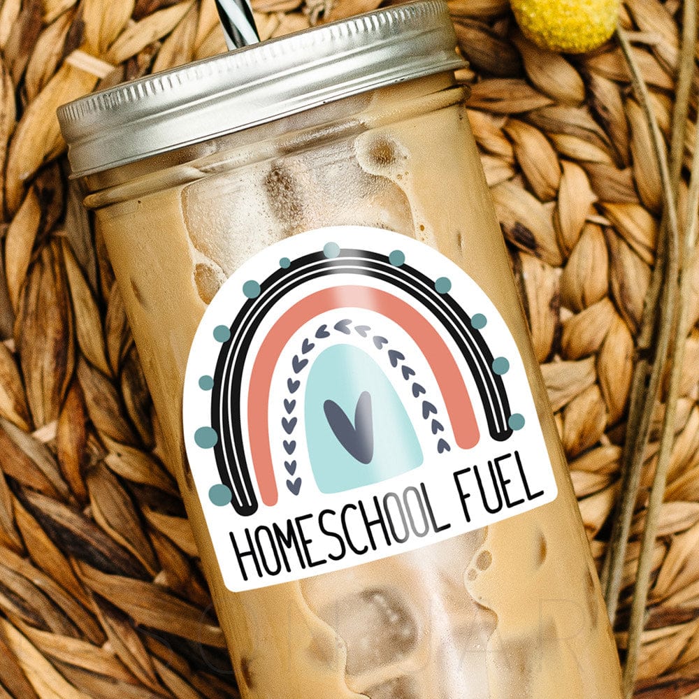 Mason jar tumbler with iced coffee, laying over a fibre mat. Tumbler reads "Homeschool Fuel" with a rainbow image.