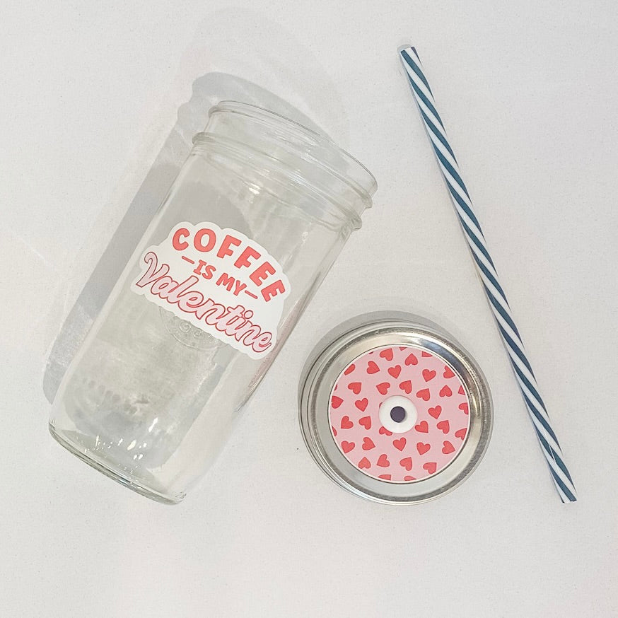 flat lay of the "coffee is my valentine" mason jar tumbler, a straw lid with red hearts on a pink background, and a black and white striped straw