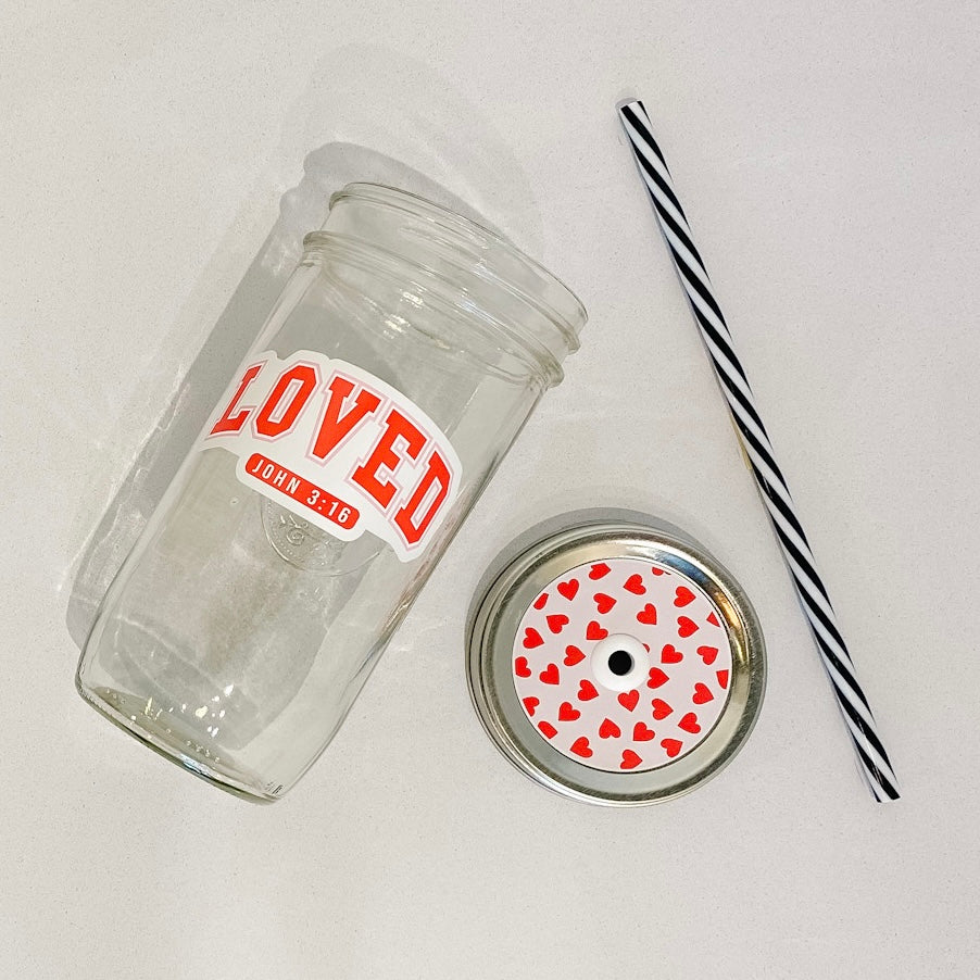 flat lay of the "LOVED John 3:16" mason jar tumbler, a straw lid with red hearts on a light pink background, and a black and white striped straw