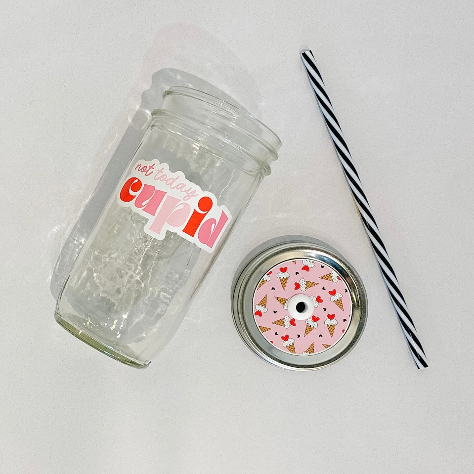 flat lay of the "not today cupid" mason jar tumbler, a straw lid that has ice cream cones on a pink background, and a black and white striped straw
