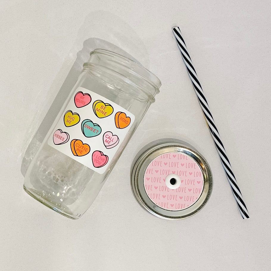 hand holding a mason jar tumbler that has 9 hearts that depict different "sweethearts" candy hearts with different valentines sayings