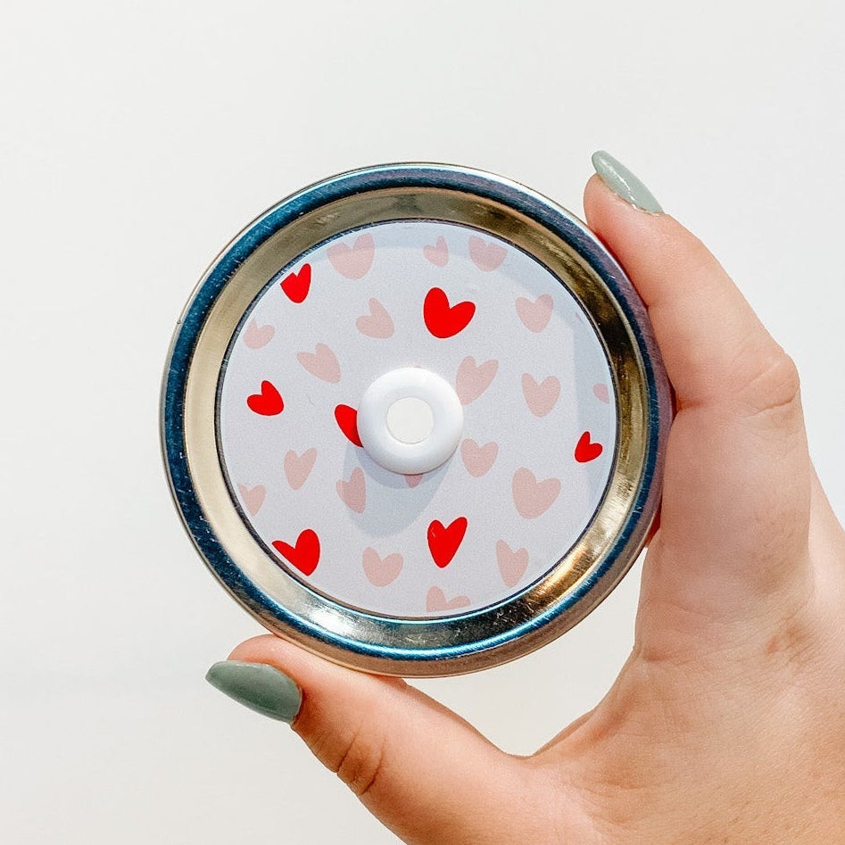 straw lid that has a pale pink background with different sized hearts in a darker pink and red spread across
