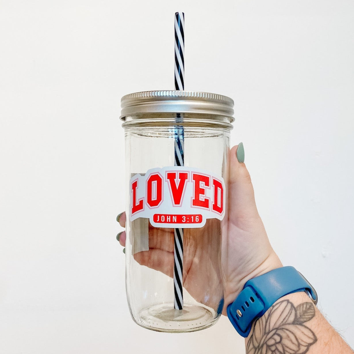 hand holding a mason jar tumbler that says "LOVED" in a blocky varsity-style font and "John 3:16" below