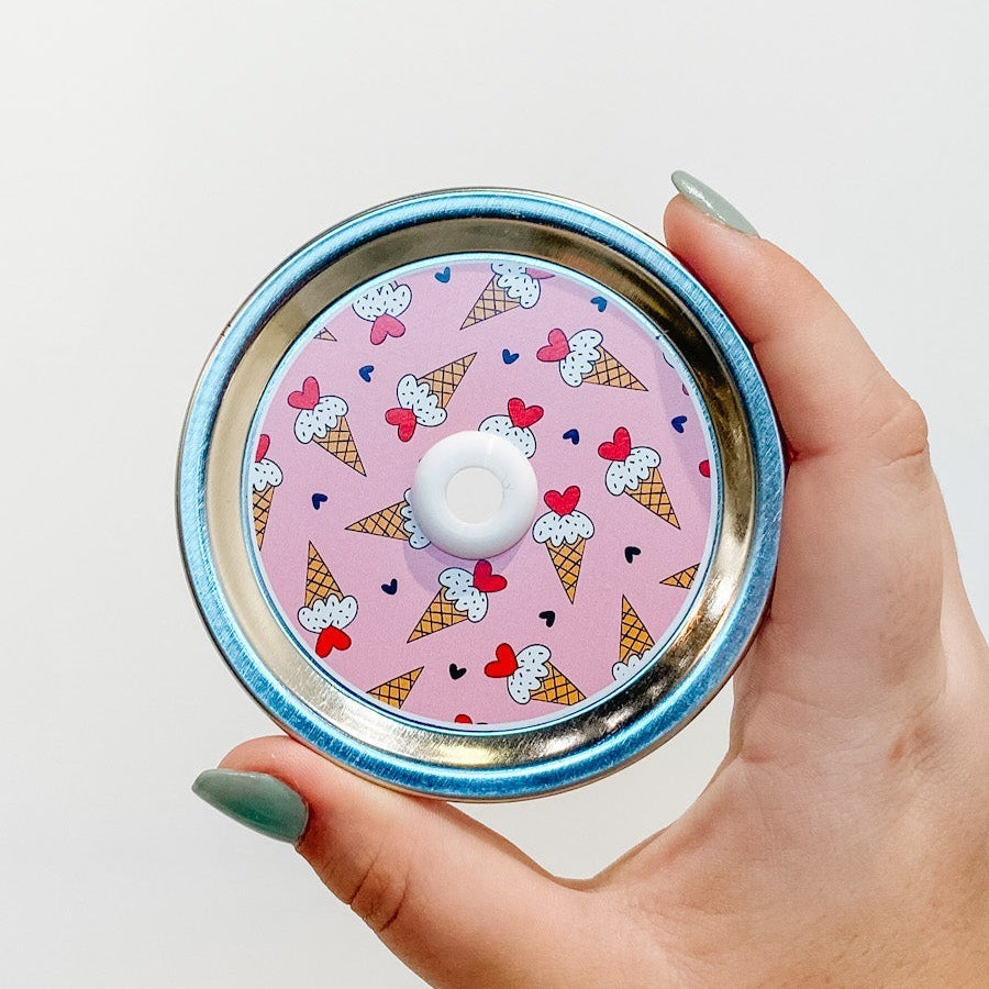 straw lid with a pink background and small ice cream cones scattered across, as well as small black hearts. The ice cream cones have a red heart in place of a cherry