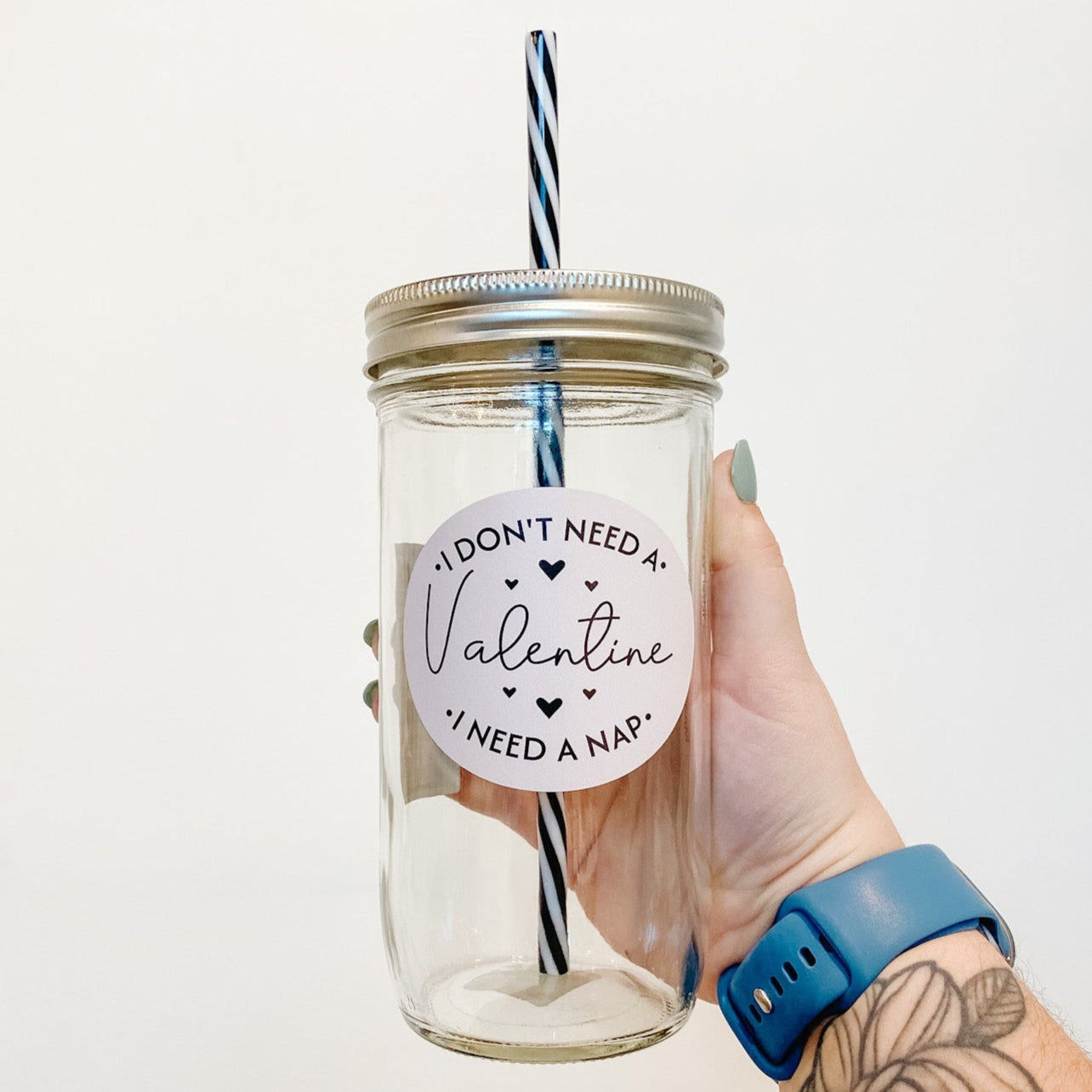 hand holding a mason jar tumbler that has a light pink circular decal that reads"I don't need a valentine, I need a nap" the wording is in black
