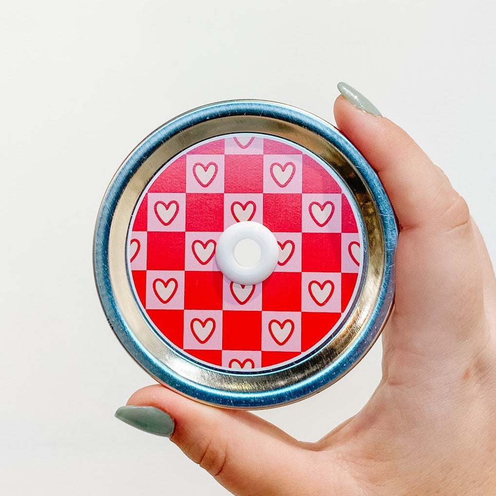 straw lid that has a pink and red checkerboard pattern, the pink squares also have a cream coloured heart in each