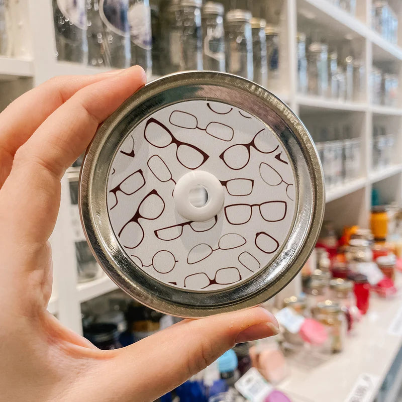 Hand holding mason jar patterned straw lid that has brown glasses on white background