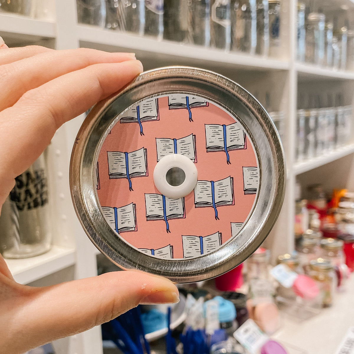 straw lid with light pink background, repeated pattern of an open book with a blue ribbon bookmark