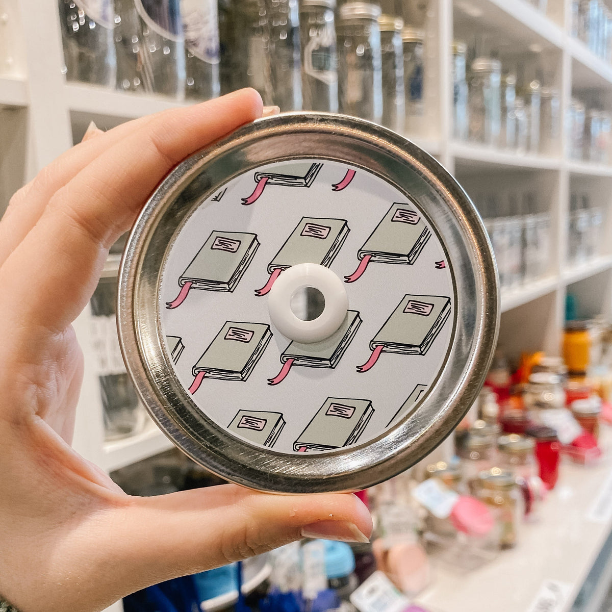 straw lid with white background and repeating pattern of closed green books with a red ribbon bookmark
