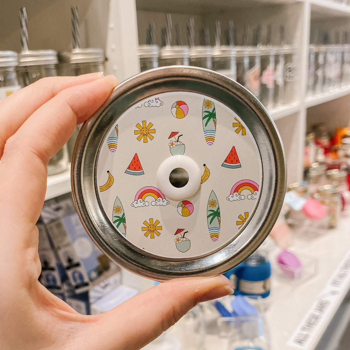 straw lid with a taupe background with watermelon slices, beach balls, surf boards, suns, drinks, and bananas patterned across