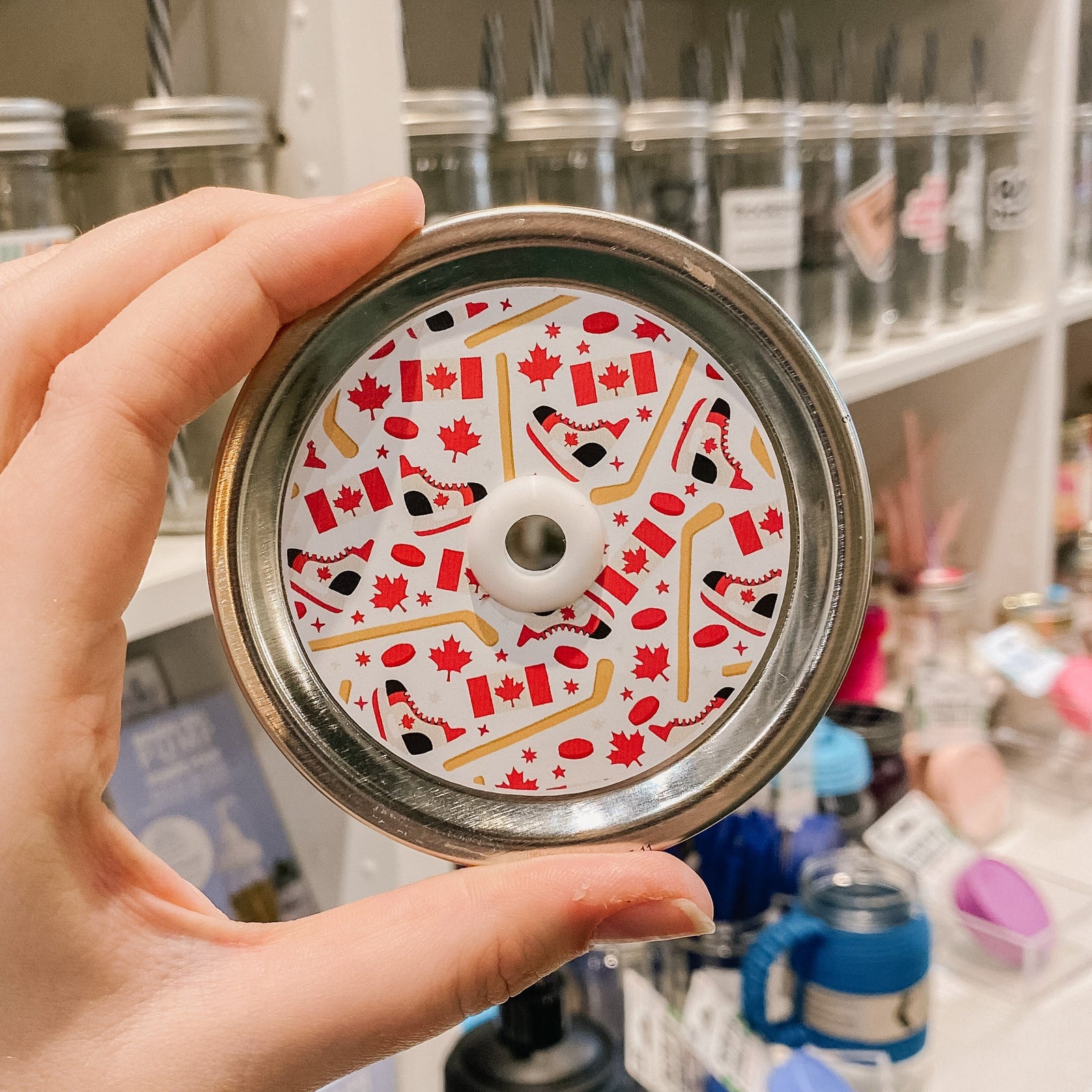 straw lid with a white background and maple leaves, canadian flags, hockey skates, hockey sticks, and pucks across the lid.