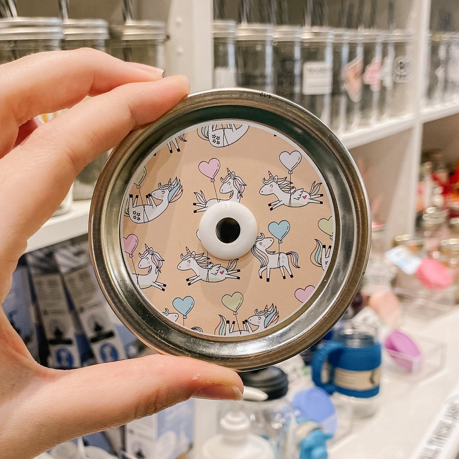 straw lid with an orange background with unicorns each being held up by a heart balloon