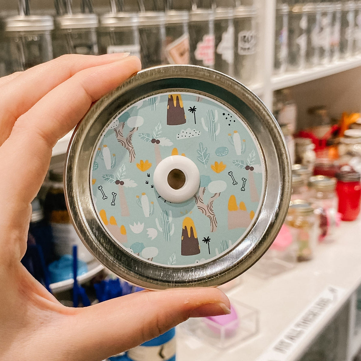 straw lid with a blue-green background, with palm trees, volcanoes, leaves, bones, and rocks on it