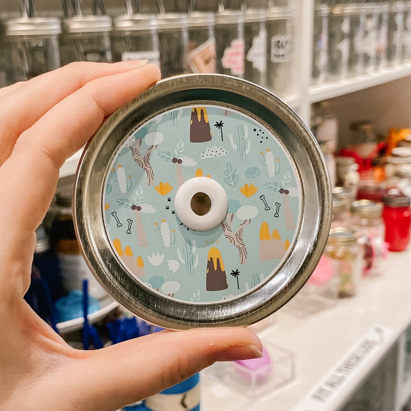 straw lid with a blue-green background, with palm trees, volcanoes, leaves, bones, and rocks on it
