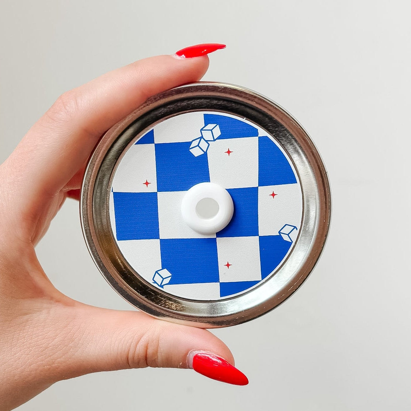 Hand holding a mason jar patterned straw lid that has blue and white checkered design with little iced cubes and tiny red stars